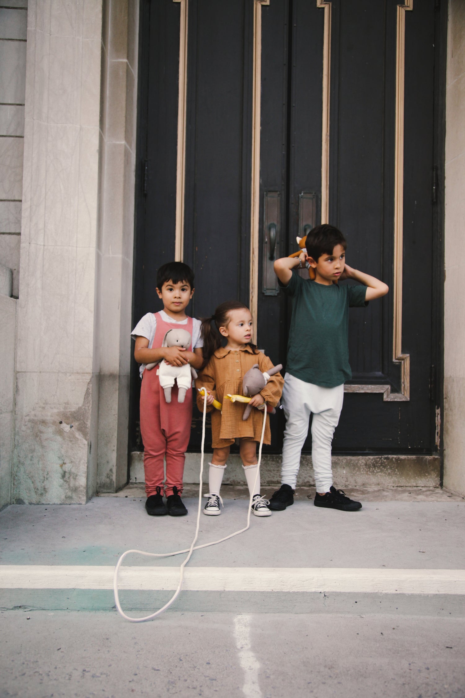 Fashionable stylish kids in european background carrying cute dolls and stuffed toys and skipping rope