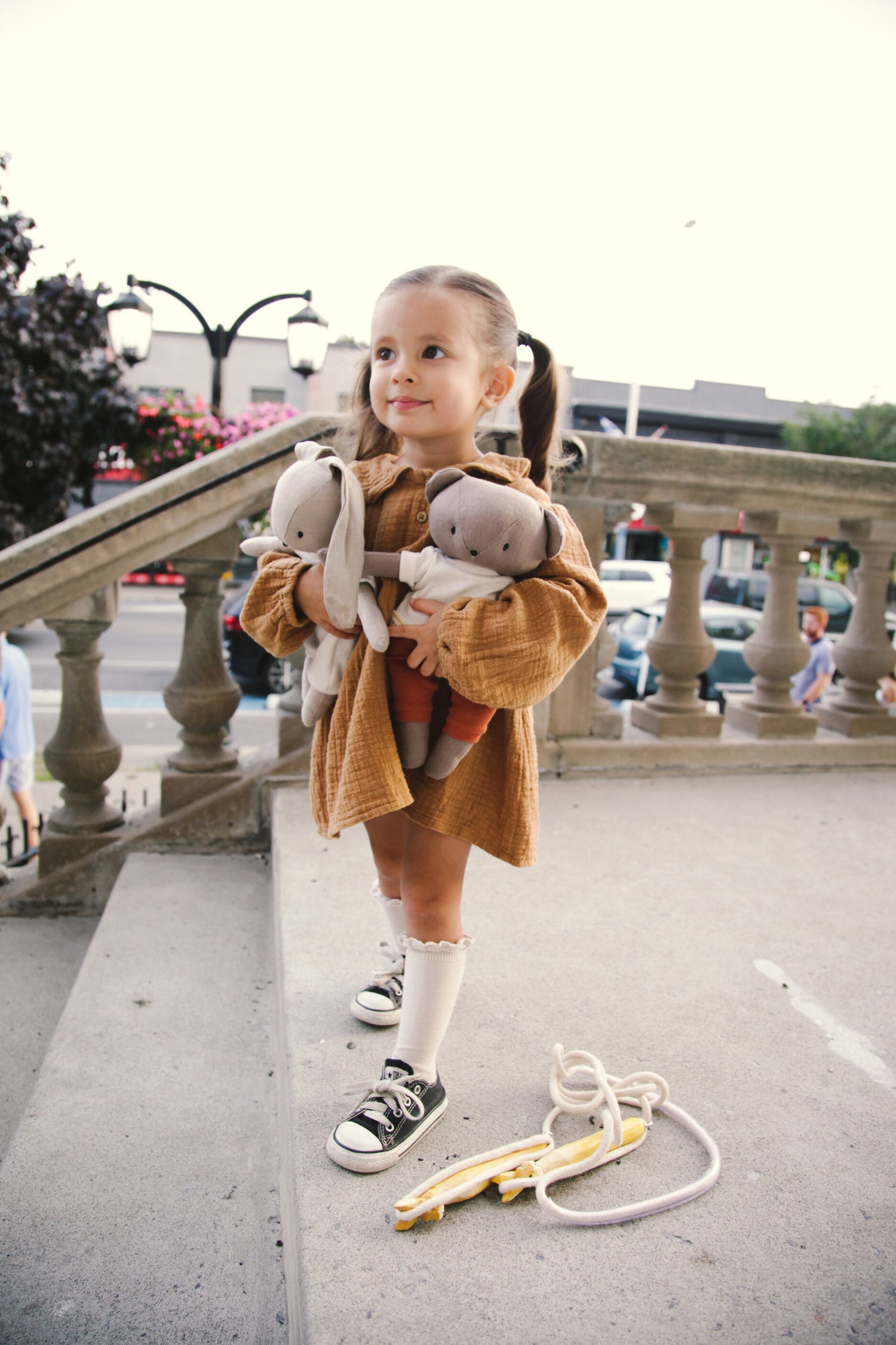 Stylish toddler girl in pig tails carrying a bunny and bear using skipping rope and wearing dress